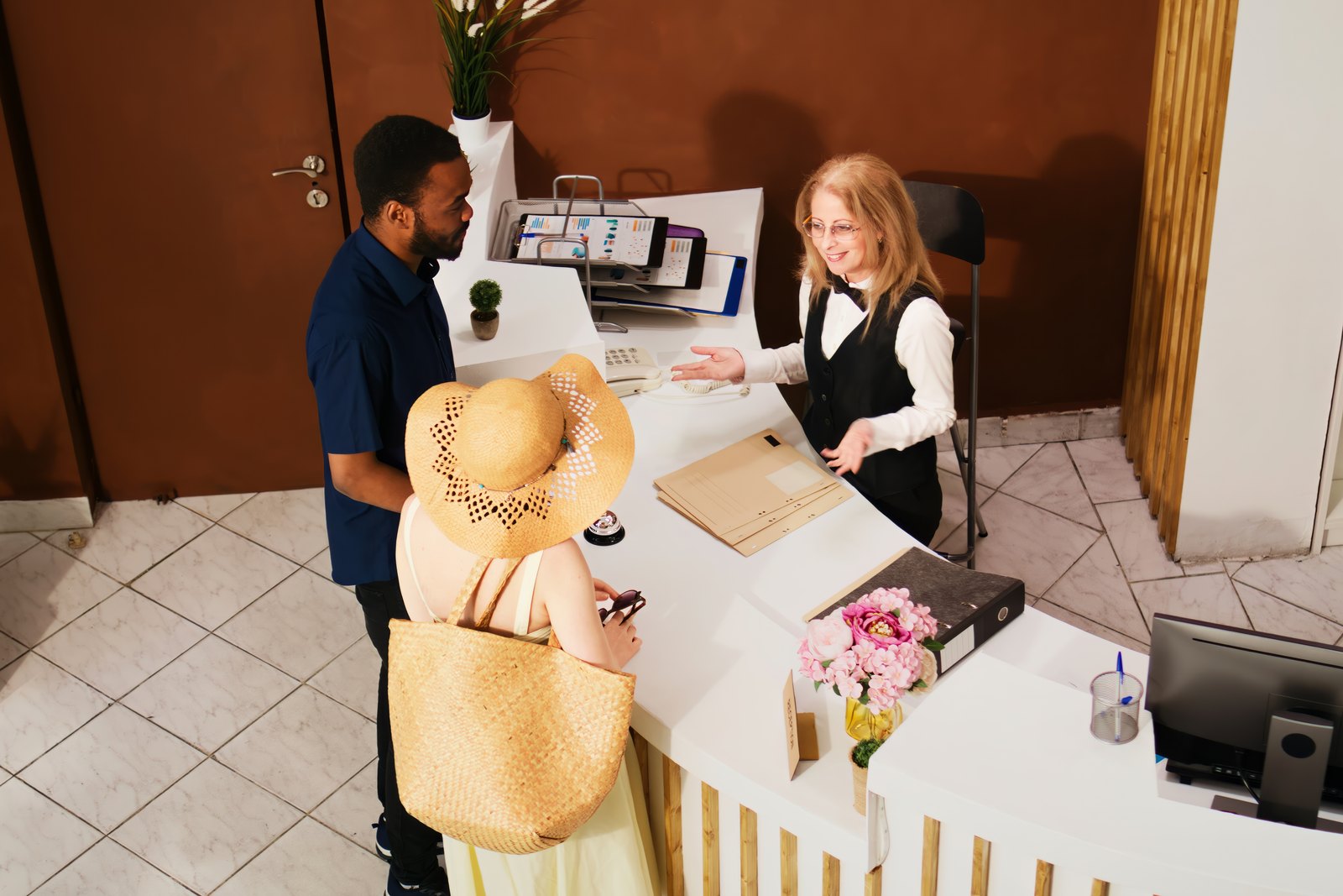 Hospedes fazendo check-in na recepcao do hotel durante feriado prolongado, com chapeu e bolsa de viagem