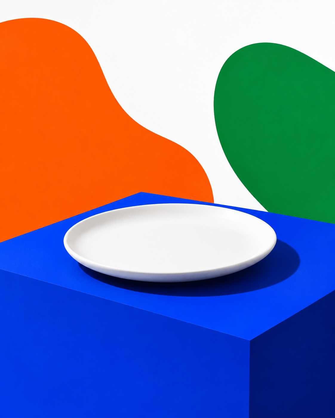 Composição conceitual de um prato branco vazio sobre bloco azul-cobalto, com formas abstratas laranja e verde ao fundo branco, sem alimento ou texto.