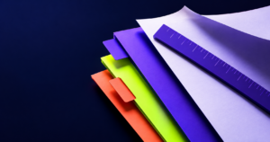 Papéis em tons roxo, lima e coral organizados sobre uma base escura em uma composição editorial abstrata.